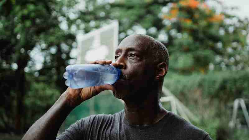 Mature African American man drinking water from a bottle in a park setting, staying hydrated., tags: te - pexel