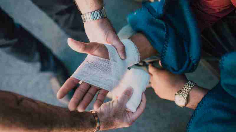 Close-up of two people bandaging an injured hand outdoors, focusing on first aid care., tags: hoe bij - pexel